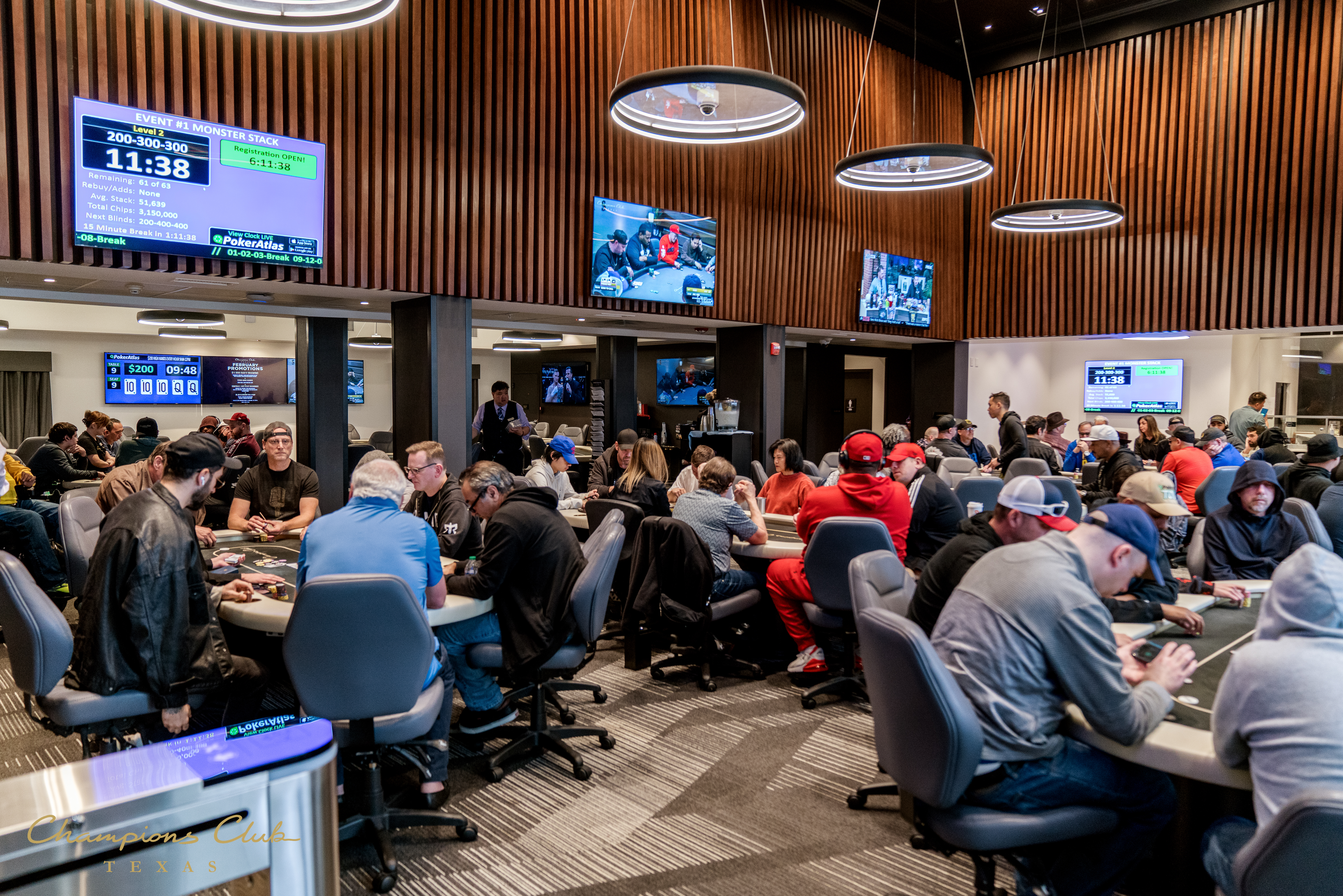 A large room filled with people sitting at poker tables under several televisions.