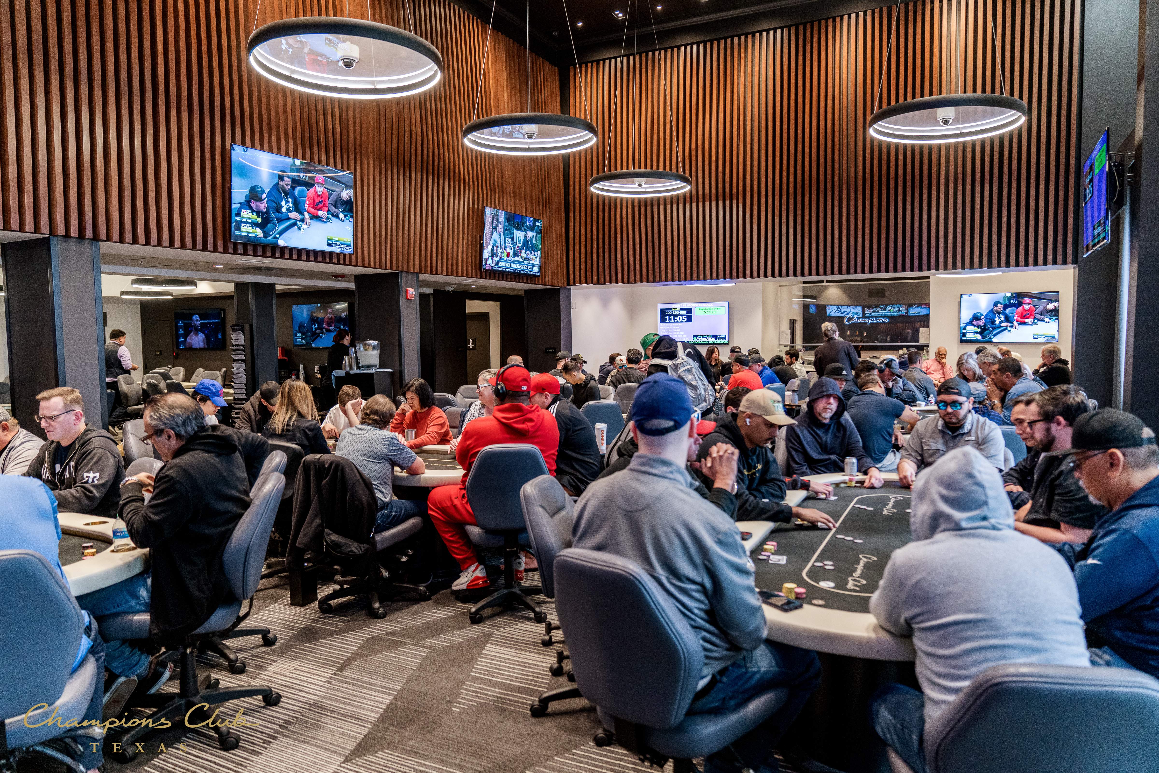 A large room filled with people sitting at tables, with multiple screens on the walls.