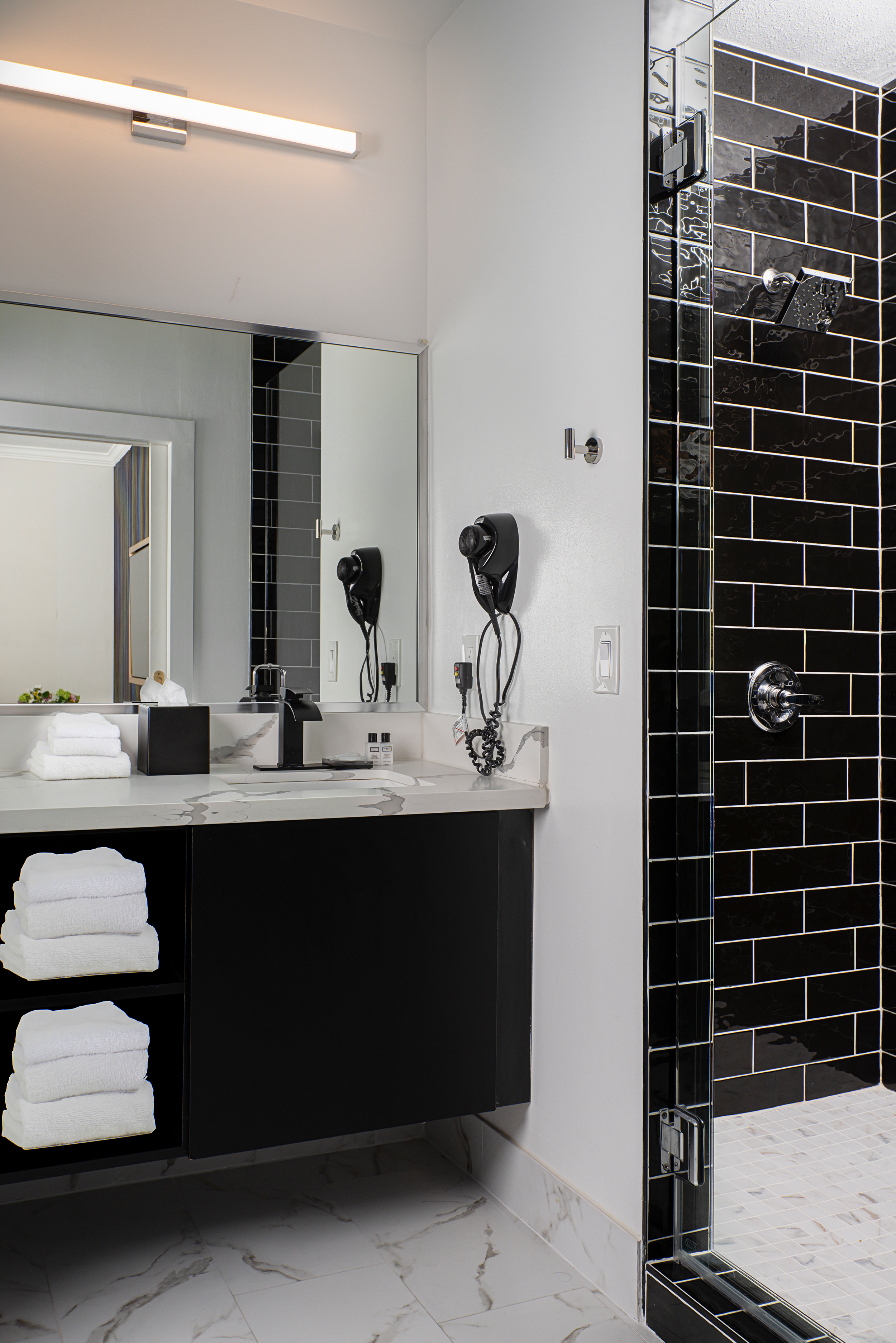 A modern bathroom with a marble countertop, black cabinets, and a tiled shower.