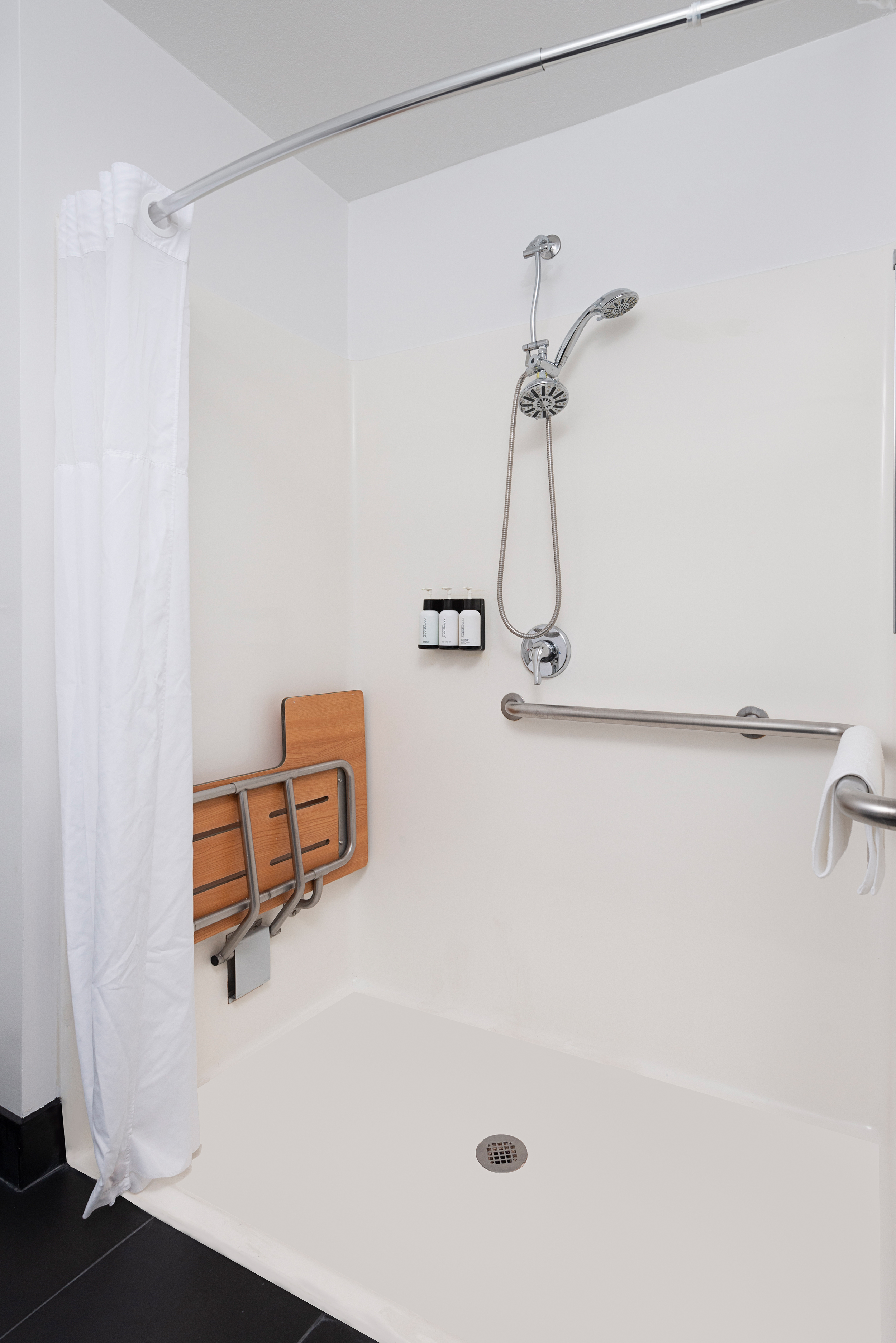 A bathroom shower with a white shower curtain, grab bars, and a silver shower head.
